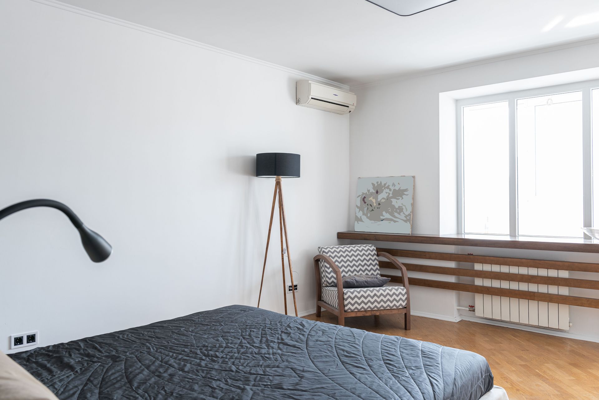 Light modern room interior with bed near lamp on floor near armchair and window near painting and air conditioner